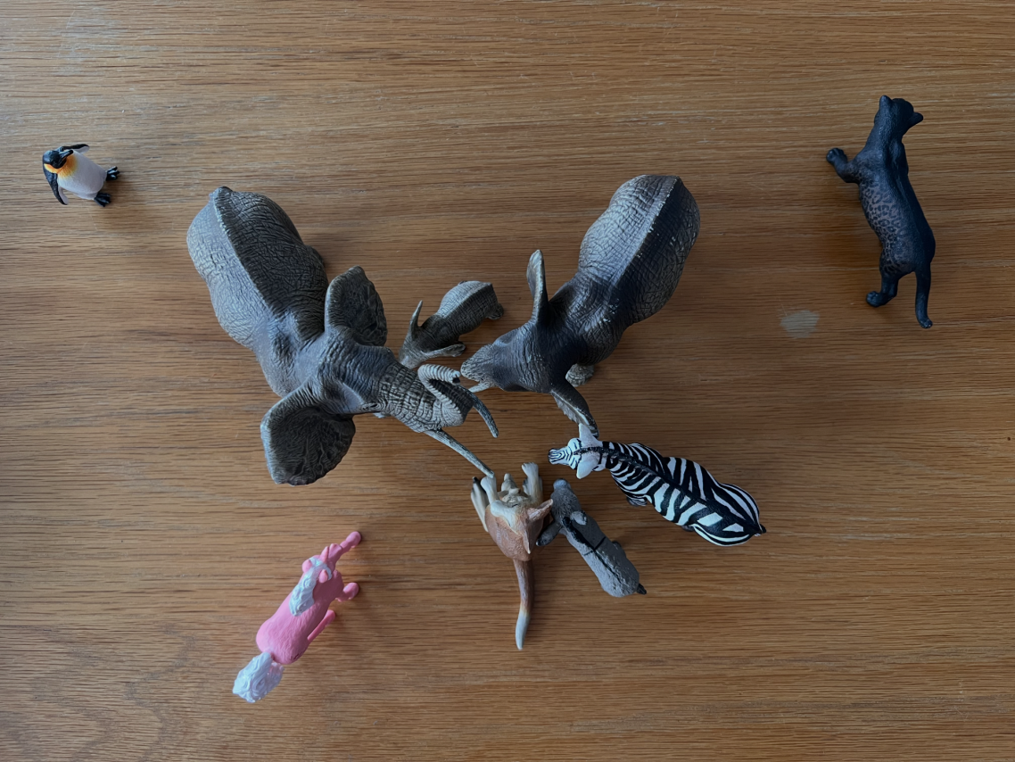 Verschiedene Spielzeugtiere und Figuren auf einer Holzoberfläche angeordnet.