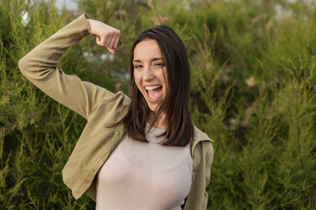 Junge Frau zeigt stolz ihren Arm, während sie fröhlich lächelt.