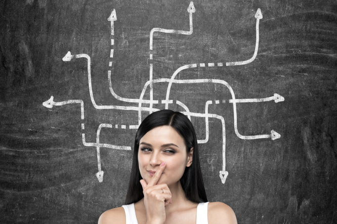 Frau mit nachdenklichem Ausdruck vor einer Tafel mit verschiedenen Pfeilen.