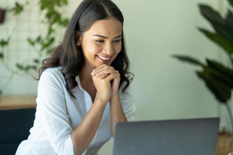 Eine Frau lächelt und betrachtet einen Laptop, umgeben von Pflanzen.